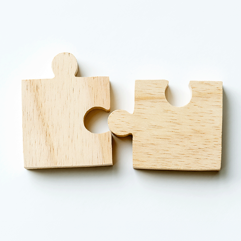 Zwei ineinandergreifende Holz-Puzzleteile als Symbol für die Verbindung von Kampagnenhandwerk und Gewerkschaftserfahrung